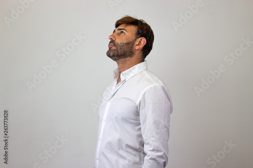 Fashion portrait of handsome young man with brown hair thoughtful, facing forwards and looking at the horizon. Isolated on white background.
