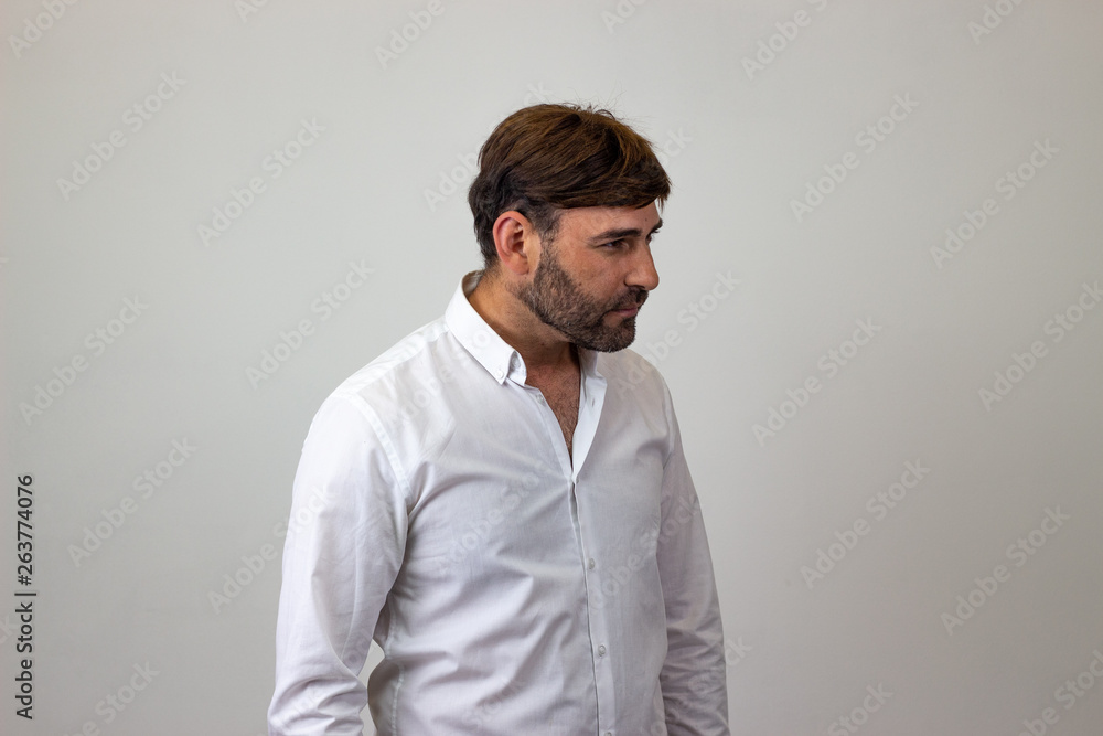 Fototapeta premium Moda portret przystojny młodzieniec z brązowymi włosami wyglądający uwodzicielsko, skierowany do przodu i patrząc z boku. Na białym tle