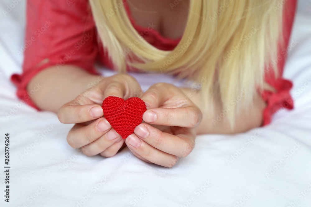 Declaration of love, red knitted heart in female hands. Blonde woman lying on the bed, concept of passion, romantic date, health care, sex or blood donation Declaration of love, red knitted heart in female hands. Blonde woman lying on the bed, concept of passion, romantic date, health care, sex or blood donation