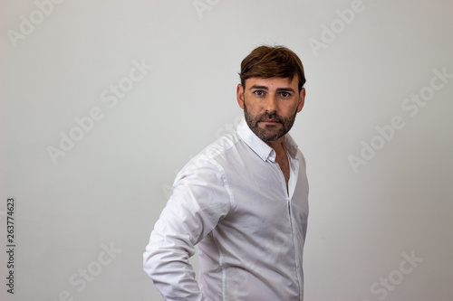 Fashion portrait of handsome young man with brown hair showing confidence, their back facing the camera and looking at the camera. Isolated on white background.