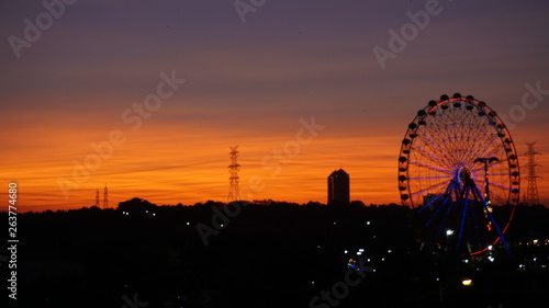 Ferris wheel at beautiful sunset. Red or orange sky background. Big ferris wheel at amusement park in orange sunset. Silhouette giant swing on twilight time of the day. Copy space. Textured wallpaper.