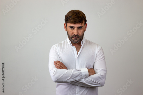 Fashion portrait of handsome young man with brown hair looking annoyed, looking at the camera. Isolated on white background.