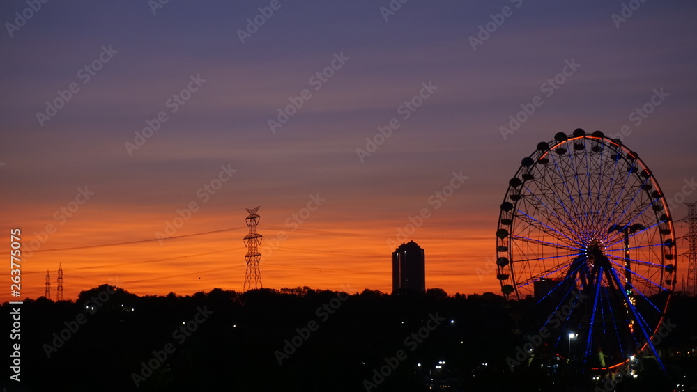 Ferris wheel at beautiful sunset. Red or orange sky background. Big ferris wheel at amusement park in orange sunset. Silhouette giant swing on twilight time of the day. Copy space. Textured wallpaper. Ferris wheel at beautiful sunset. Red or orange sky background. Big ferris wheel at amusement park in orange sunset. Silhouette giant swing on twilight time of the day. Copy space. Textured wallpaper.