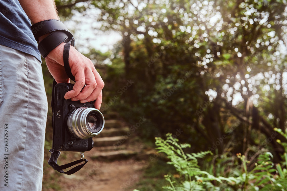 Fototapeta premium Man is holding camera in his hand while walking by the path throw the green mountains