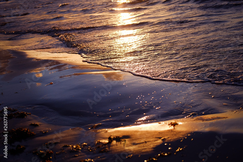 Fototapeta Naklejka Na Ścianę i Meble -  Reflection of sunset in seashore with warm golden light, clouds and bright blue sky