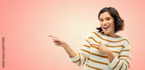 people concept - happy smiling young woman in striped pullover pointing fingers to something over living coral background