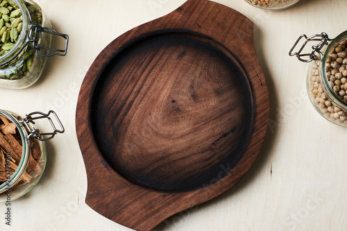 Empty round wooden tray, cordamom, cinnamon bark, nuts and pepercorns in glass jars. photo