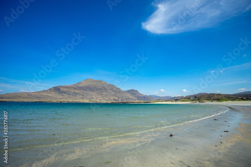 une grande plage déserte aux eaux bleues turquoises et des montagnes en arrière plan 