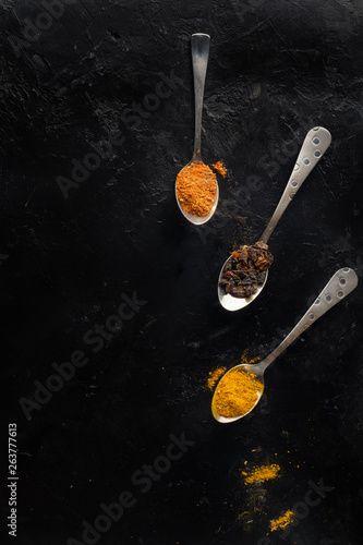 Various colorful spices on black background, top view.