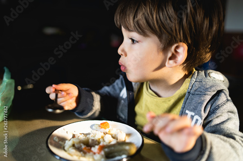 Portrait of a little boy eating having lunch by the table at home