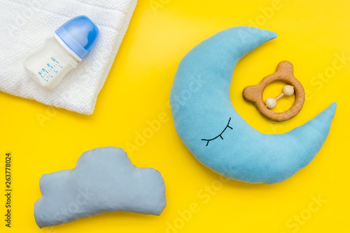 Baby care concept with moon pillow, clouds, feeding bottle and toy for sleep of newborn on yellow background top view