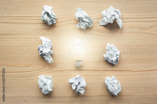 Many crumpled white paper balls with one light bulb between them. Concept of think different, think out of the box, leadership.