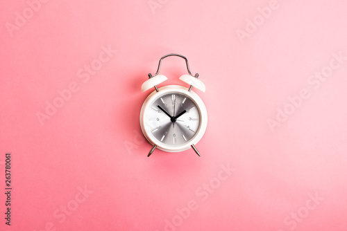 Retro white and silver alarm clock on a pink background. Time concept, top view, flat lay 