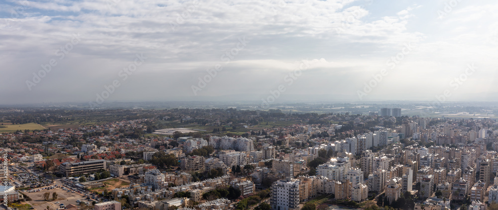 Aerial panoramic view of a residential neighborhood in a city during a cloudy and sunny sunrise. Taken in Netanya, Center District, Israel.