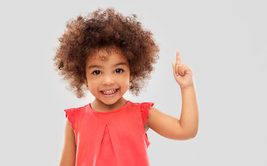 idea, warning and childhood concept - happy little african american girl pointing finger up over grey background