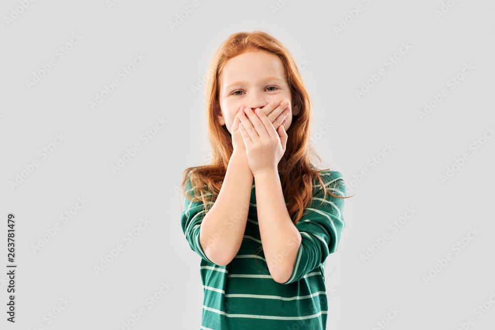 childhood, embarrassment and emotions concept - confused red haired girl in green striped shirt covering her mouth by hands over grey background childhood, embarrassment and emotions concept - confused red haired girl in green striped shirt covering her mouth by hands over grey background