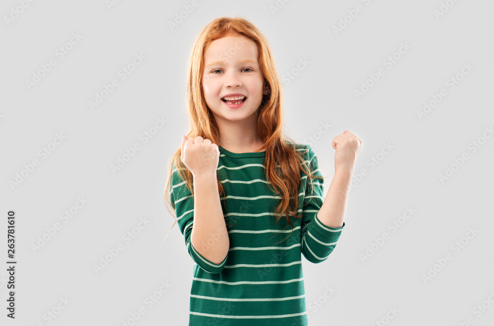 childhood, gesture and people concept - smiling red haired girl in green striped shirt celebrating success over grey background childhood, gesture and people concept - smiling red haired girl in green striped shirt celebrating success over grey background