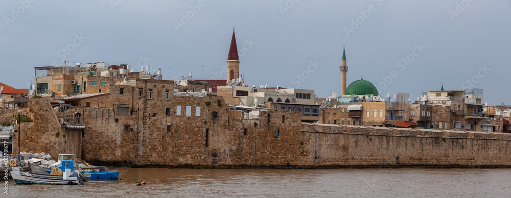 Fototapeta premium Beautiful Panoramic view of the Old City of Akko on the coast of Mediterranean Sea during a cloudy and sunny day. Taken in Acre, Israel.