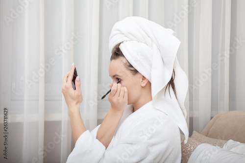 Young pretty european woman in bathrobe takes care of her skin and body after shower. Make up brush. Getting ready for work doing morning makeup. Skin moisturizing. Close up.