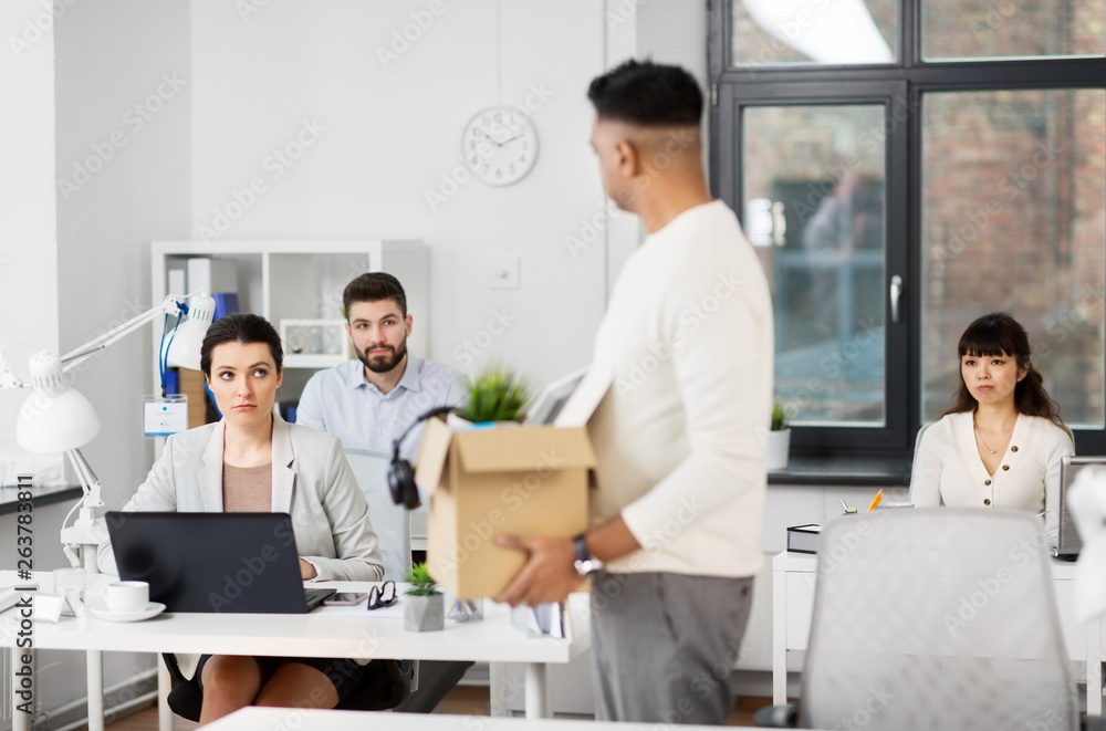 business, firing and job loss concept - sad office workers looking at fired male colleague with box of personal stuff business, firing and job loss concept - sad office workers looking at fired male colleague with box of personal stuff