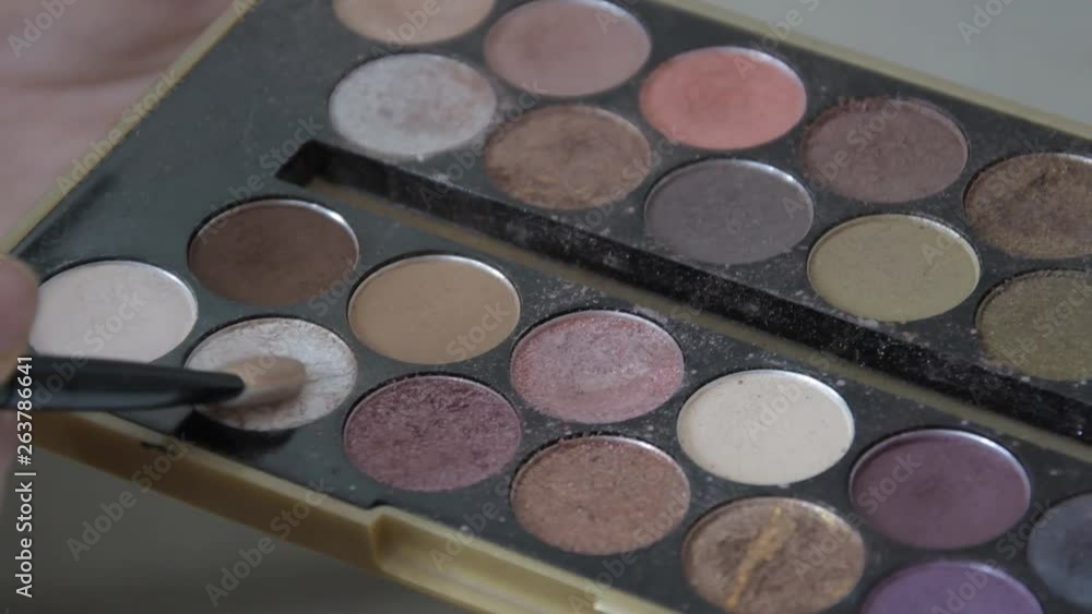 Young woman holding multicolor palette of eyeshadows in hand while make up artist work with her face. Closeup of colourful professional set of eye shadows for beautiful make-up. Young woman holding multicolor palette of eyeshadows in hand while make up artist work with her face. Closeup of colourful professional set of eye shadows for beautiful make-up.