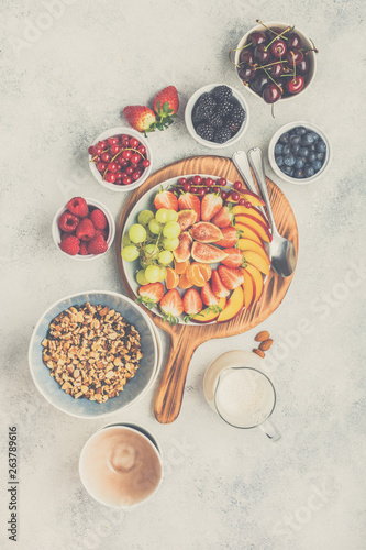 Raw vegan grain free paleo style granola or muesli made from nuts. Fruit berries platter, strawberries blueberries raspberries peach figs red currant, overhead view, toned, selective focus