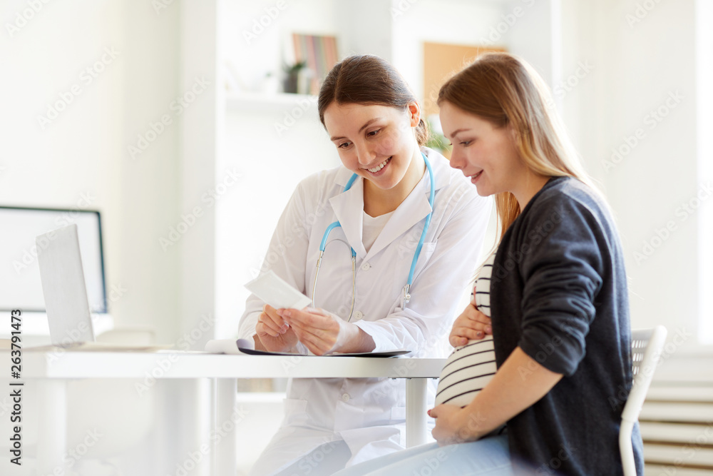 Portrait of pregnant young woman looking at ultrasound picture while visiting obstetrician, copy space Portrait of pregnant young woman looking at ultrasound picture while visiting obstetrician, copy space