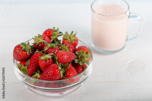 Fresh strawberry in a bowl and glass of milk on wooden background.