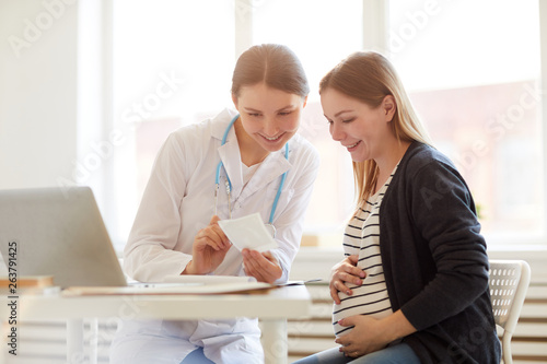 Portrait of smiling female obstetrician consulting pregnant woman in doctors office, copy space photo
