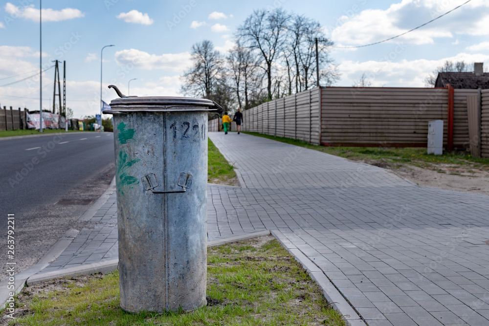 Old trash bin standing on the sidewalk by the road in the city. Metal bucket for municipal waste. Old trash bin standing on the sidewalk by the road in the city. Metal bucket for municipal waste.