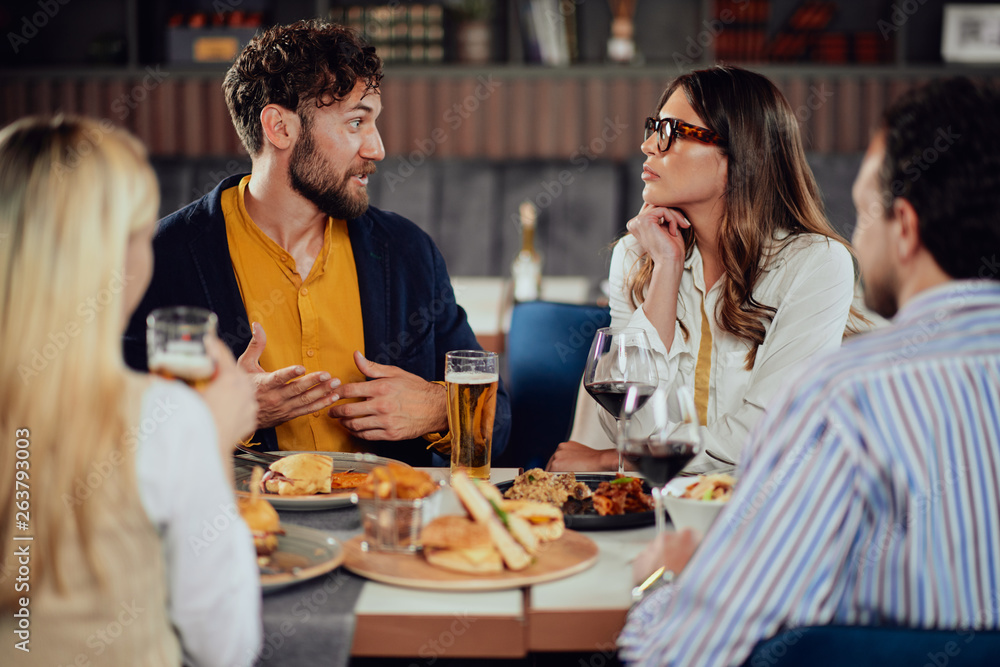 Multiethnic friends sitting at restaurant, drinking alcohol, chatting and having burgers for dinner.