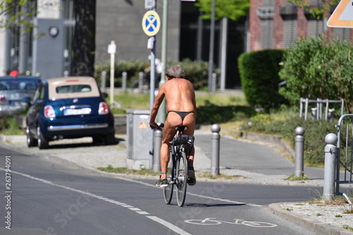 An almost naked elderly man with gray hair rides a bicycle on a warm and sunny spring day in Berlin Germany