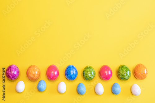 A lot of colorful Easter eggs on a yellow background. Top view, minimal Easter concept. Happy Easter card with free, empty space.