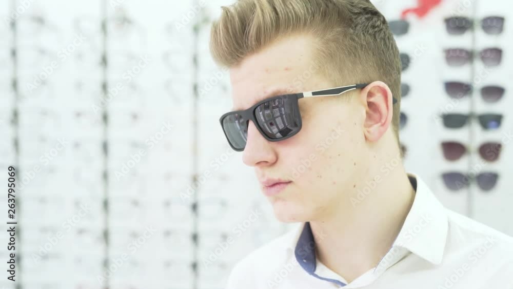 Young Man Trying On Sunglasses While Posing And Running Hand Through Hair Young Man Trying On Sunglasses While Posing And Running Hand Through Hair