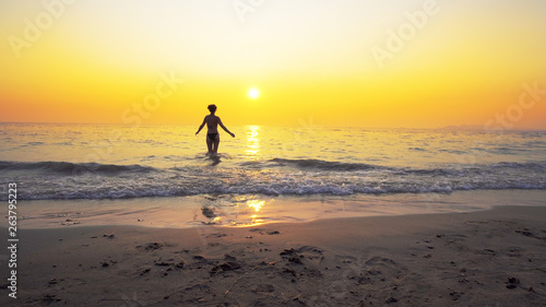 Sexy fit model go in the sea water toward amazing sunset