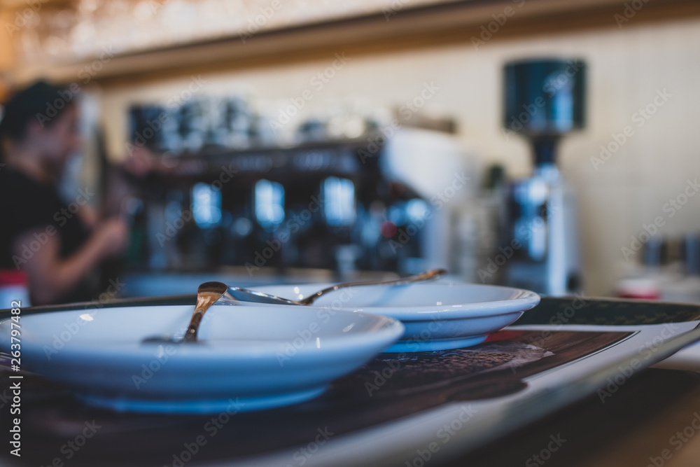 Empty saucers with spoons in the foreground of a cafe with bokeh coffee machine in the background. 