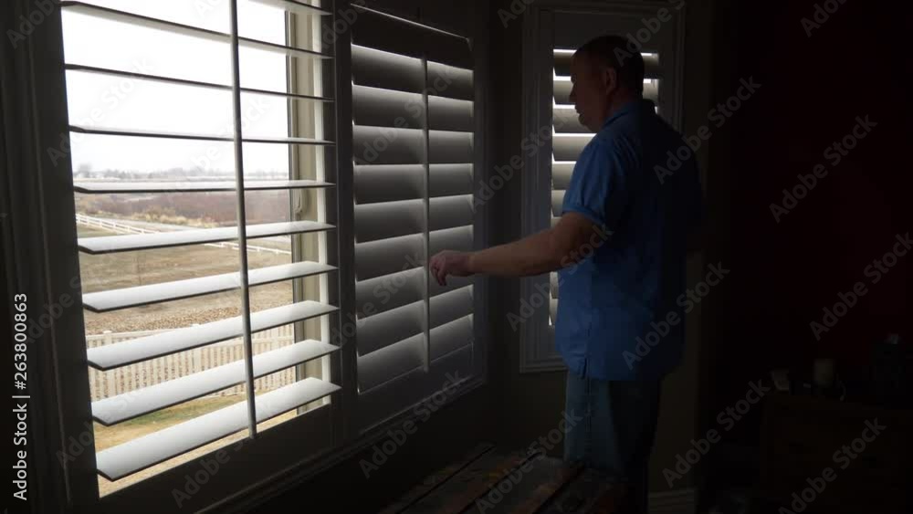A sad and depressed older man looks out the window from a dark room then closes the blinds A sad and depressed older man looks out the window from a dark room then closes the blinds