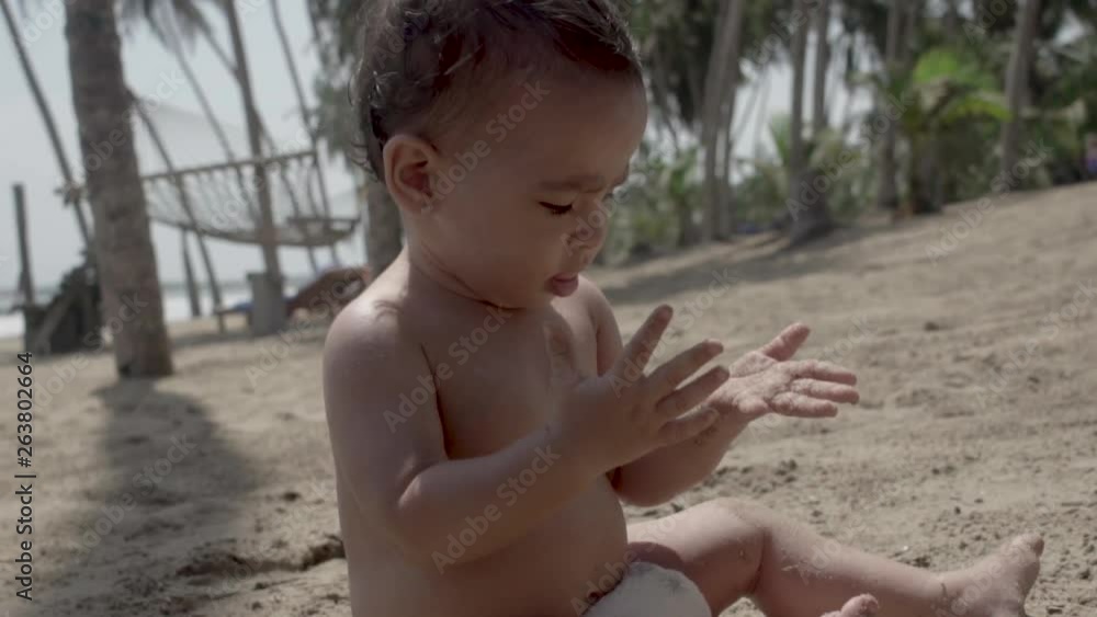 Seated baby playing with the sand on the beach of a resort Seated baby playing with the sand on the beach of a resort