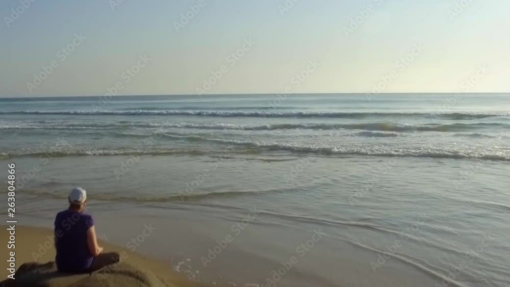 Aerial drone shot moving low past woman sitting on rocks Aerial drone shot moving low past woman sitting on rocks