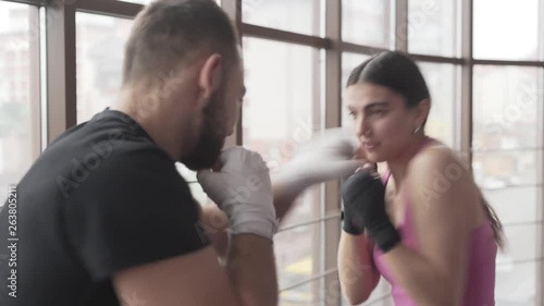 Male and female boxers train in the gym. They do jab punches and imitate a slight hand-to-hand combat. They practice non-stop on a very professional level. Blurred background. photo