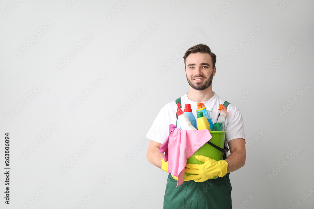 Portrait of male janitor with cleaning supplies on light background Portrait of male janitor with cleaning supplies on light background