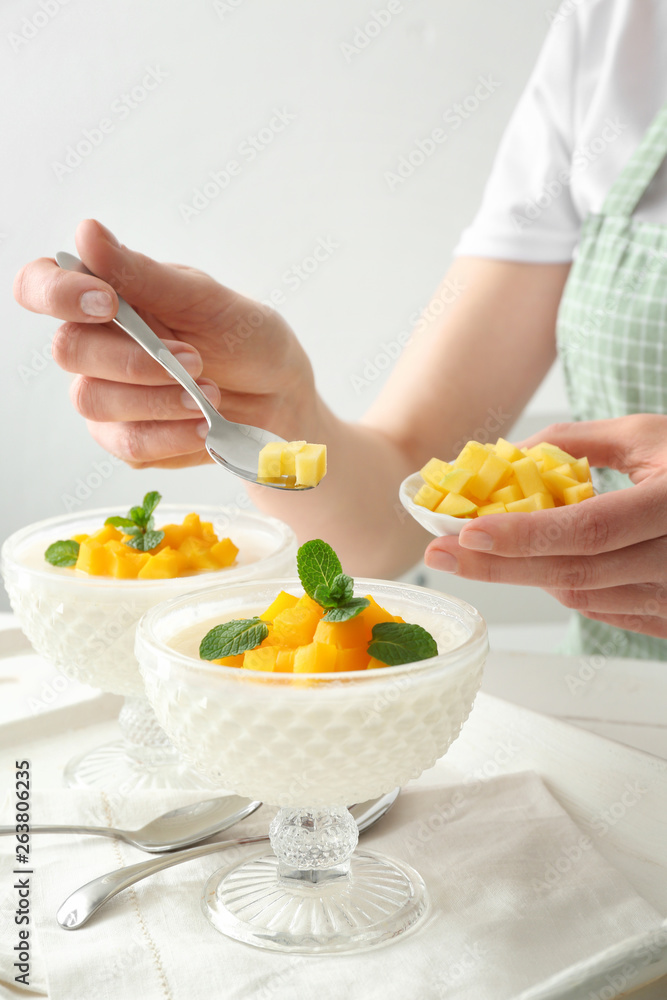 Woman decorating tasty panna cotta at table