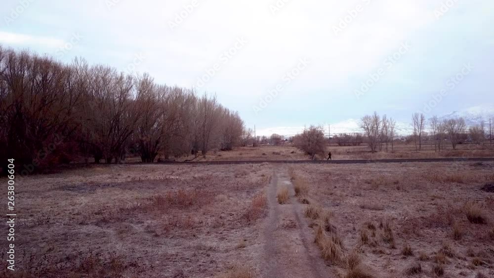 View of a lonely trail with a man walking away wearing hat and backpack View of a lonely trail with a man walking away wearing hat and backpack