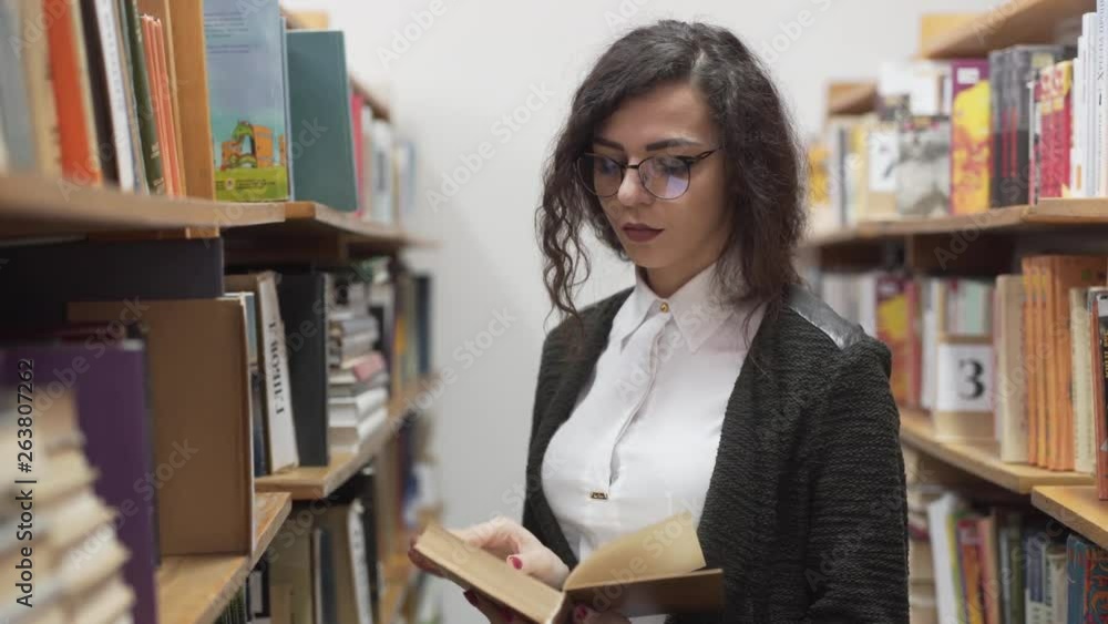 Beautiful librarian reads a book in the stacks of a library.