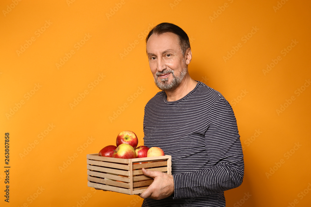 Portrait of handsome mature farmer with apples in box on color background Portrait of handsome mature farmer with apples in box on color background