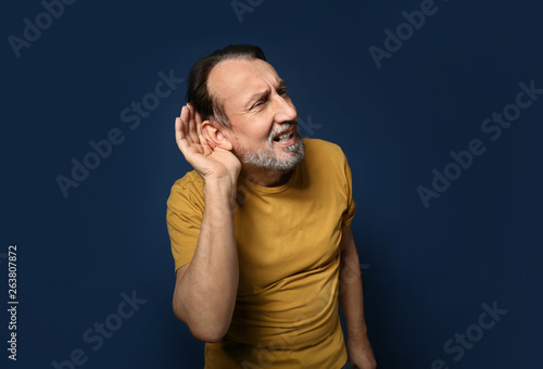 Portrait of handsome mature man with hearing problem on color background