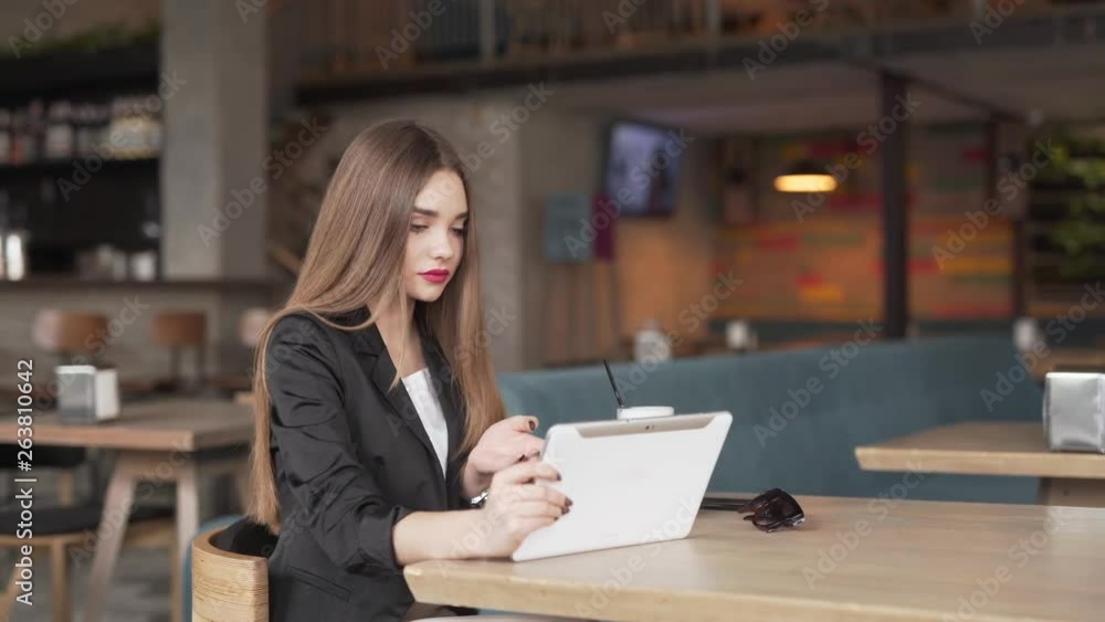 Young businesswoman uses her tablet device to talk on a video conference call while sitting in a coffeeshop. Young businesswoman uses her tablet device to talk on a video conference call while sitting in a coffeeshop.