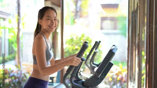 Beautiful Petite Asian Woman Working Out in Gym With Big Windows and Natural Light. She Looks at The Camera and Smiles photo