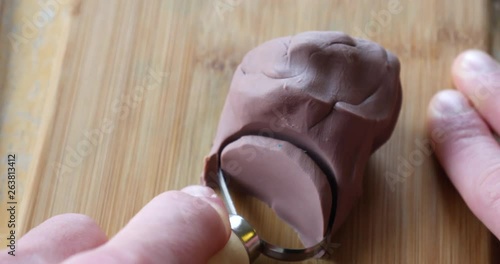 Close up on the hands of an artist or sculptor cutting and carving a soft brown modeling clay sculpture with a tool on a wood desk in an art studio. photo