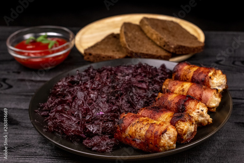 Fried homemade grilled sausages or chevapchichi with stewed sauerkraut, and slices of rye bread and tomato sauce on a wooden rustic background